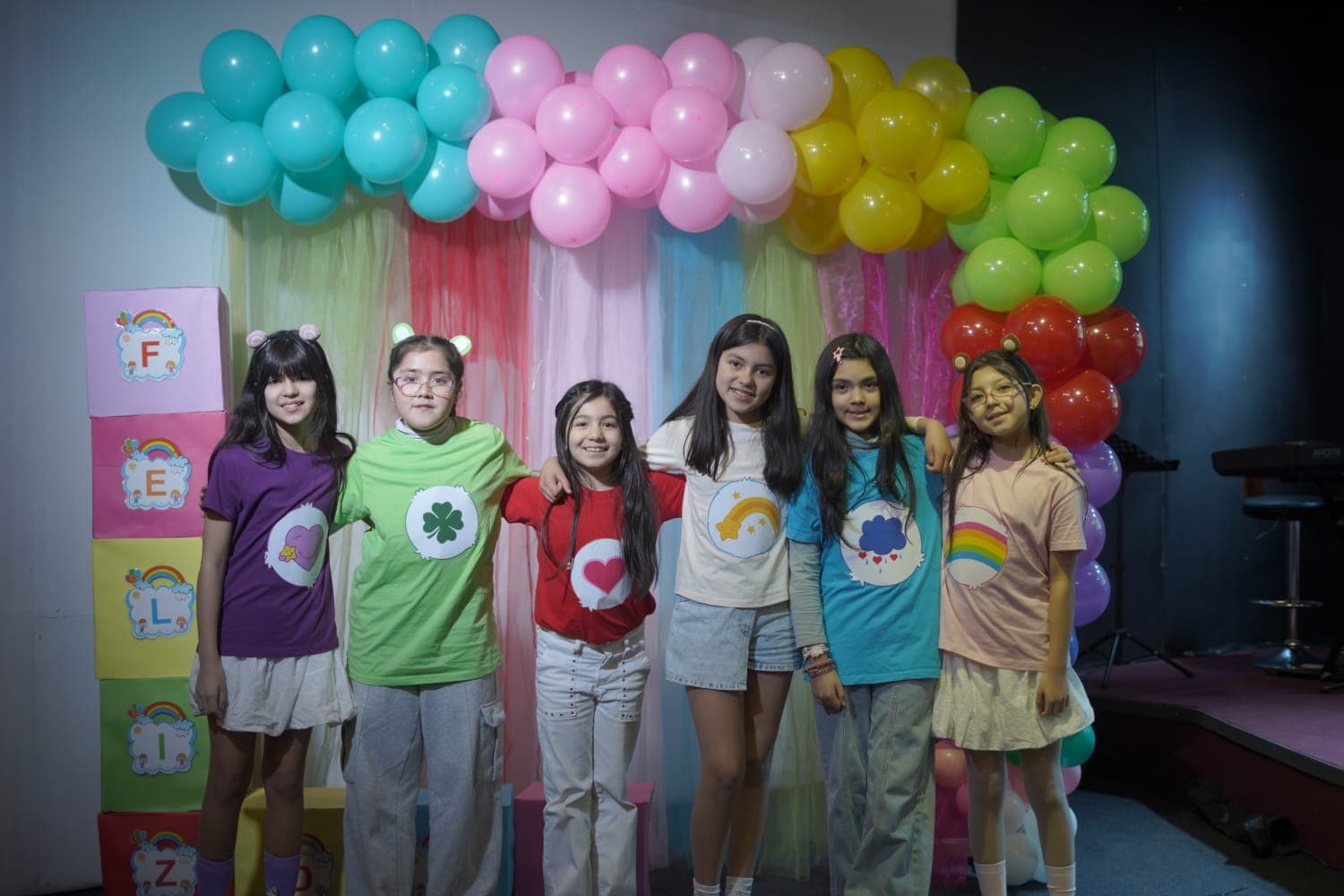 Niñas con poleras de colores frente al arco de globos