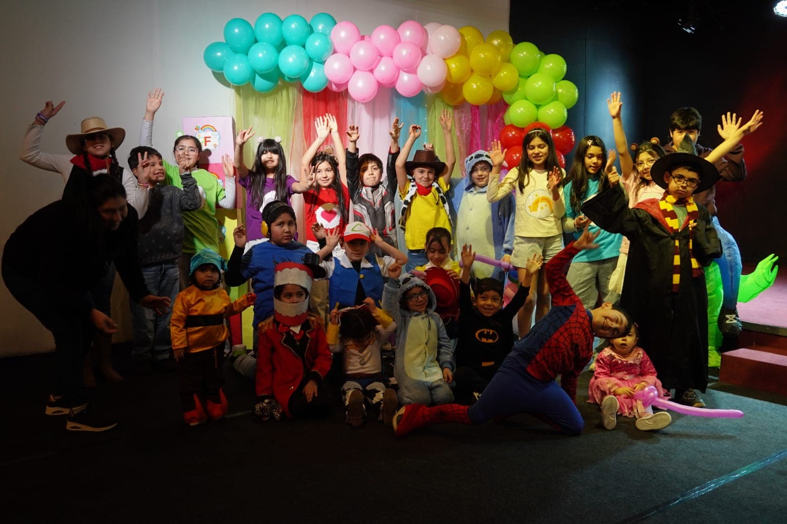 Niños y niñas disfrazados celebrando frente a un arco de globos de colores